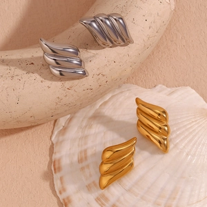 Macro detail of textured 18K gold and silver layered wing earrings on organic props