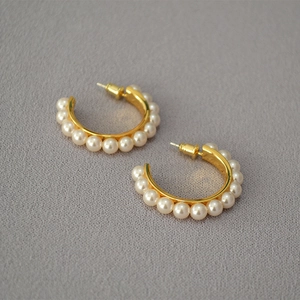 Detailed close-up of gold-plated hoop earrings with elegant white pearls on gray fabric