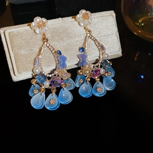 Macro detail of luxury floral fringe earrings with blue teardrop charms on velvet stand