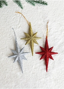 Detail of red, gold, and silver glitter star ornaments on snowy background with pine needles