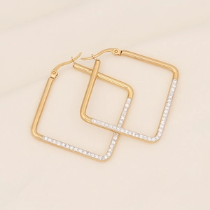 Macro shot of gold square earrings with white rhinestones on beige fabric background