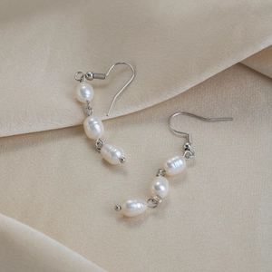 Detailed view of baroque pearl drop earrings on a soft beige silk fabric background