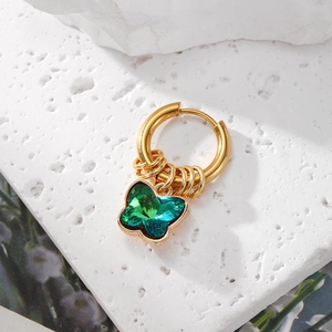 Macro detail of a gold butterfly hoop earring with green crystal on a stone texture