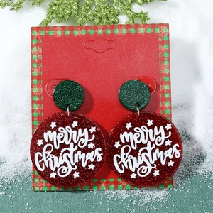 Détail de boucles d'oreilles de Noël pailletées rouge et vert avec texte sur branche de pin