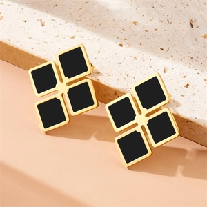 Macro detail of gold earrings with black square inlay on a textured stone background