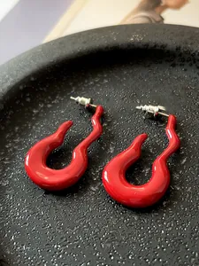 Macro shot of red enamel wave stud earrings in a gray ceramic bowl with artistic flair