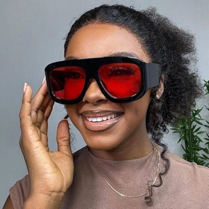 Detail of square black frame sunglasses with vibrant red lenses worn by a model