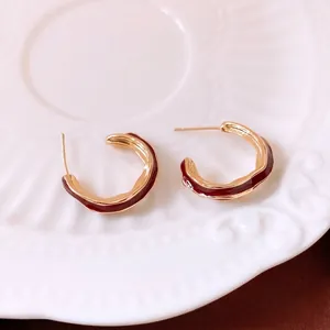 Gold-plated C-shaped wavy hoop earrings with burgundy enamel on white ceramic tray