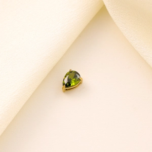 Macro shot of green pear-cut zircon pendant with gold prong setting on silk fabric
