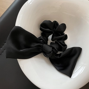 Detail of a black satin scrunchie with large bow knot inside a white ceramic bowl