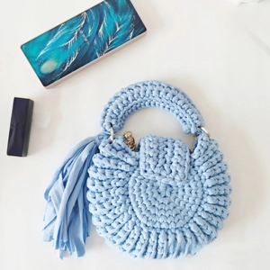 Macro shot of light blue hand-woven crochet bag with round fringe and metallic chain strap