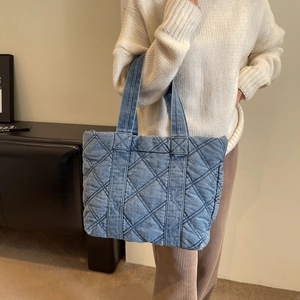 Sac cabas en jean bleu matelassé à motif de losanges, porté par un mannequin en intérieur