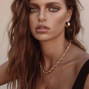Detail of chunky gold rope chain necklace and hoop earrings on model with warm tones