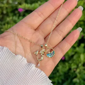 Detail of 18K gold plated mermaid and blue sea stone pendants on a thin cross chain