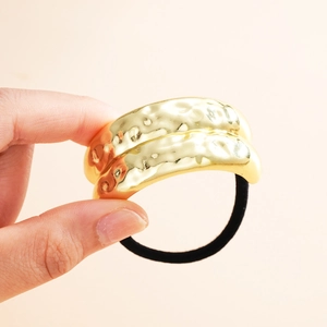 Close-up of golden wave-textured metal bead on black elastic hair tie ponytail holder