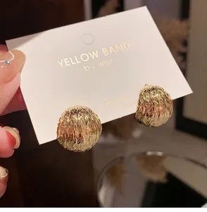 Close-up of golden dome earrings featuring textured ripple patterns on a display card