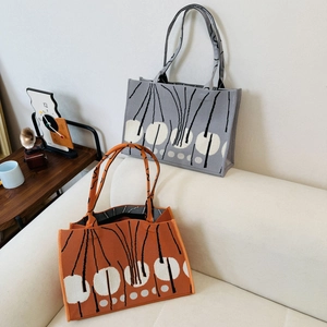 Close-up of grey and orange knitted tote bags with abstract tree patterns and vertical textures