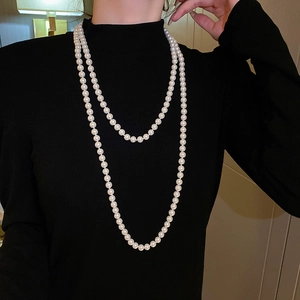 Detail of layered long pearl necklace on black sweater showing elegant white luster
