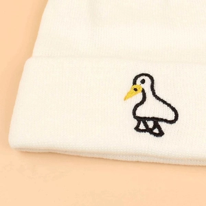 Detailed close-up of a white knit beanie featuring a small embroidered duck on the cuff