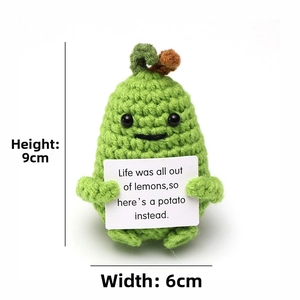 Close-up of a green handmade crochet cucumber doll holding a positive message card
