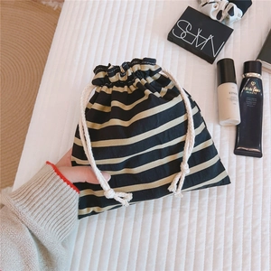 Detail of a black and yellow striped cotton drawstring pouch held on a textured surface