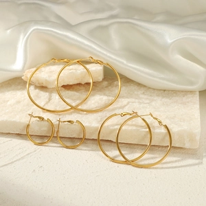 Three pairs of golden stainless steel hoop earrings in varied sizes on white silk