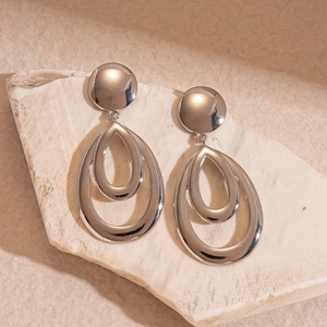 Close-up of silver-toned metallic layered hollow teardrop earrings on a textured stone surface