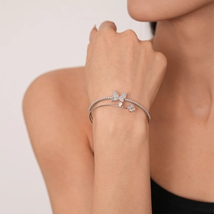 Close-up of double-layer silver bangle with pavé butterfly and flower charms on wrist