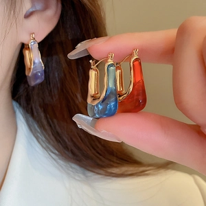 Macro detail of U-shaped acrylic earrings in blue and red with gold metallic accents