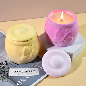 Detalle de frascos de cerámica para velas con relieves de mariposas en amarillo y rosa