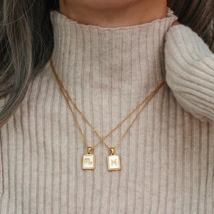 Detail of gold Scorpio and Pisces shell necklaces worn by a model on a beige sweater