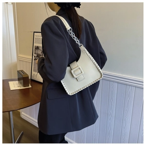 Close-up of cream shoulder bag featuring woven edges and decorative square buckle