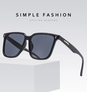 Macro view of black oversized sunglasses with gold metal temple details on a white base