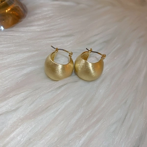 Close-up of golden irregular hoop earrings with matte metal texture on soft white fur
