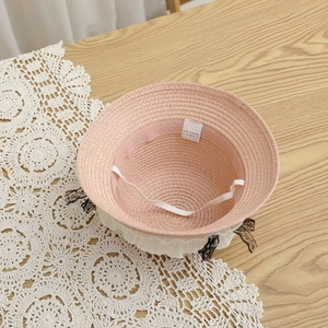 Détail du chapeau de paille rose montrant l'étiquette 100% papier et bord en dentelle
