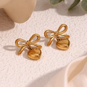 Détail des boucles d'oreilles nœud et cœur plaquées or 18 carats sur fond texturé