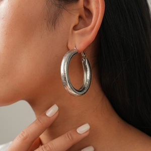 Close-up of large silver geometric hoop earrings with glitter texture on a female model