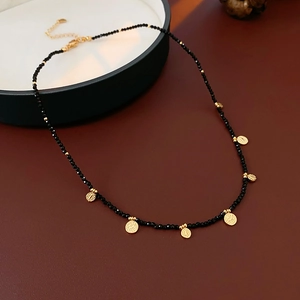 Gros plan d'un collier de perles noires avec pendentifs disques dorés sur cuir rouge