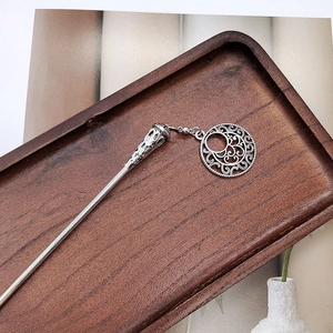 Detail of silver Chinese hair pin with hollow pendant on a dark wooden tray