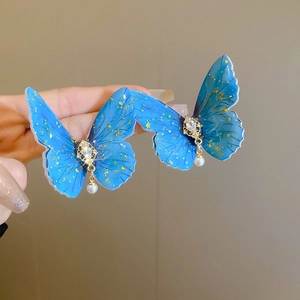 Detail of blue acrylic butterfly earrings with gold foil, crystal and pearl drop charms