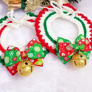 Detail of hand-knitted Christmas pet collar with a golden bell and bow on plush white fur