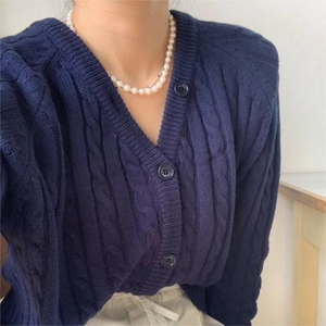 Close-up of navy blue cable-knit cardigan with V-neck and pearl necklace accessory