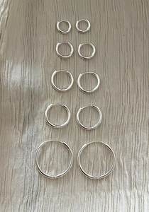 Five pairs of polished 925 sterling silver hoop earrings in varying sizes on silk cloth