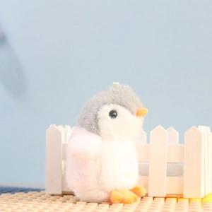 Close-up of cute plush penguin keychain with gray, pink and white soft fur texture