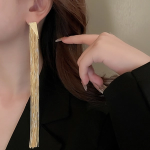 Detail shot of long gold tassel earrings with triangle studs worn by a female model