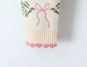 Detail of knit sweater cuff with bow pattern, ribbed texture and pink wavy edges