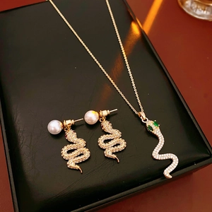 Dettaglio del set di gioielli a serpente dorato con occhi di gemma verde e perle