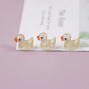 Detailed macro of three mini glowing resin ducks with gold glitter inside and orange beaks