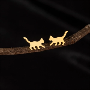 Polished gold walking cat silhouette stud earrings displayed on a dark rustic branch