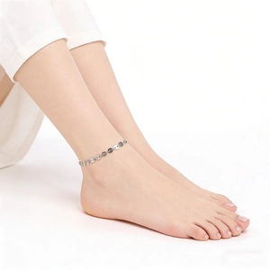 Detail shot of a silver stainless steel pig nose chain anklet on a woman's ankle.